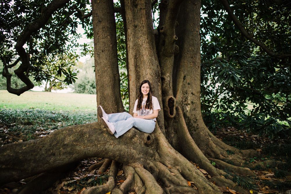 Young woman sitting peacefully among large exposed roots of a massive tree in green park.