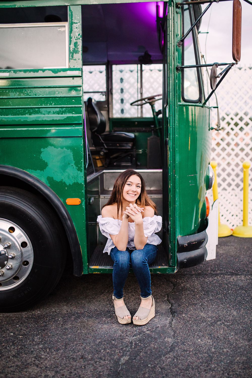 Smiling young woman sitting in doorway of vintage green bus holding a small item.