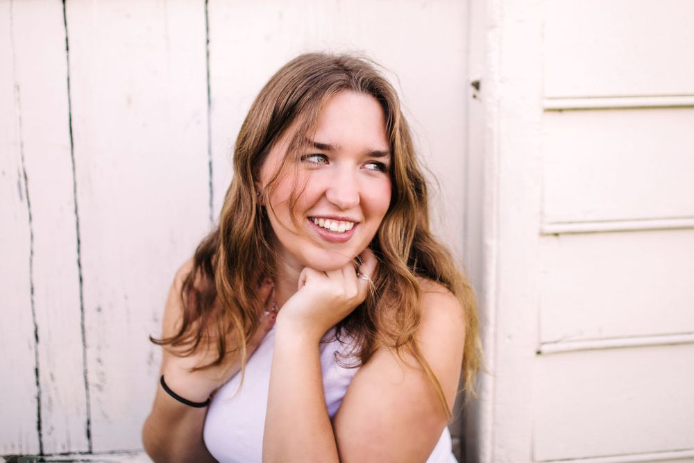 Happy young woman with brown hair laughing while leaning against a white wooden door.