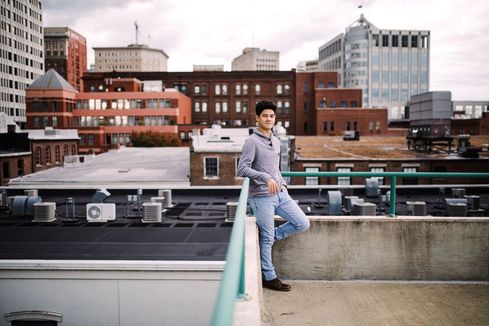 Young man leaning on rooftop railing with expansive city skyline behind him.