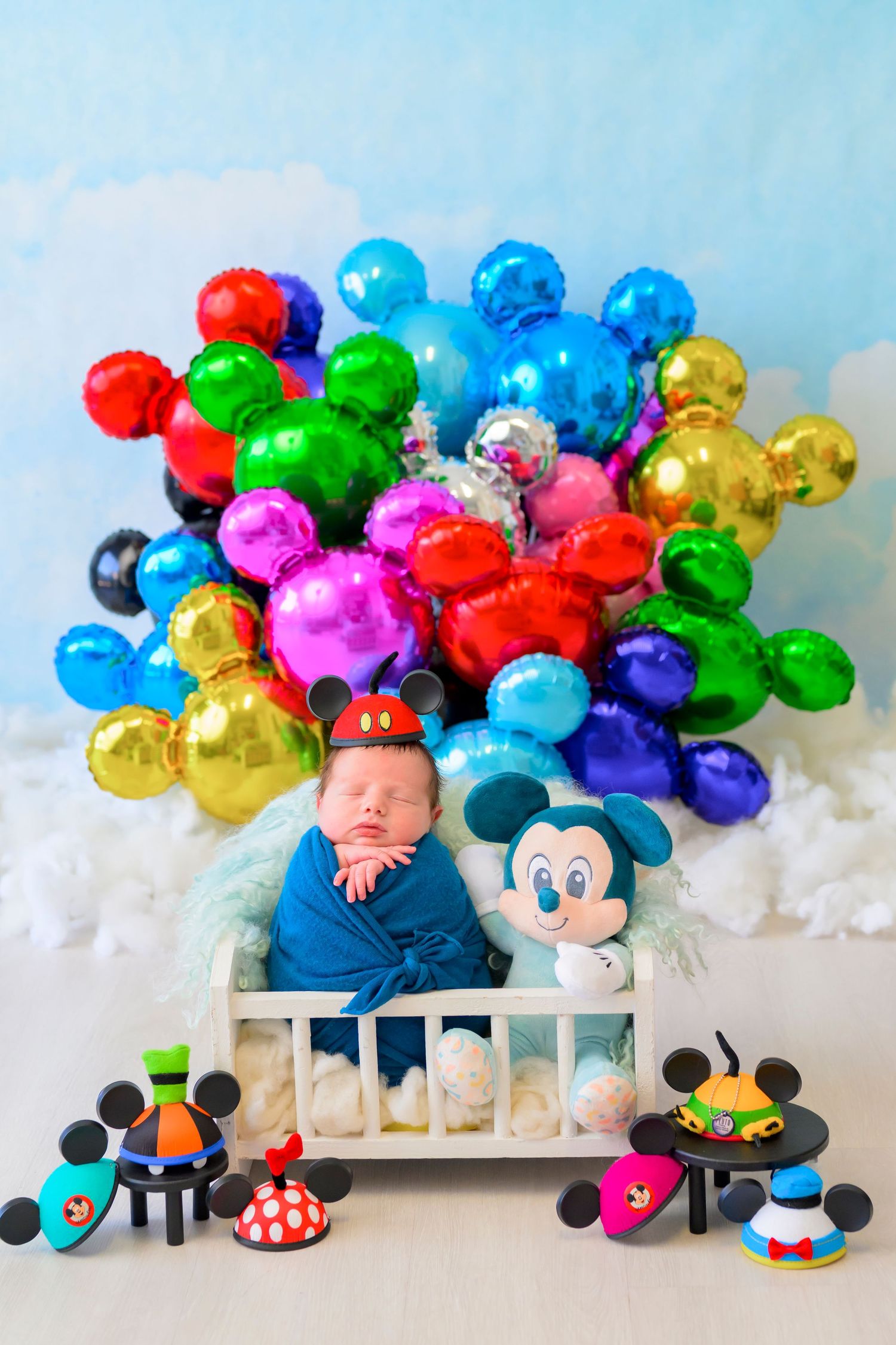 Colorful balloon display with Mickey Mouse toys and soft cotton clouds creates a whimsical Disney-themed photo setup.