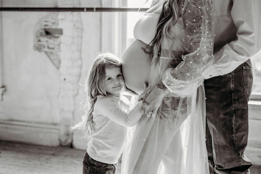 Sweet black and white maternity moment with small child touching dress.
