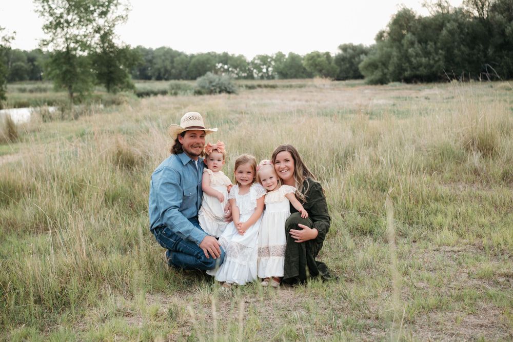 Candid family moment captured in a grassy field with rustic backdrop.