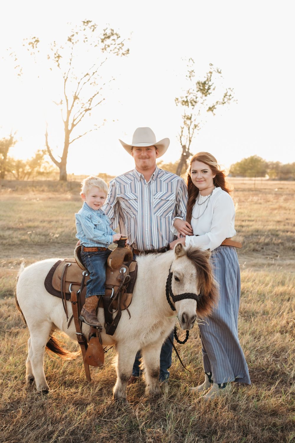 Family poses with their white pony in a rustic field at sunset.