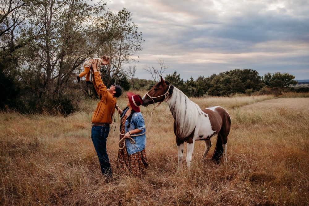 Family enjoying a sunset moment with their horse in a golden field.
