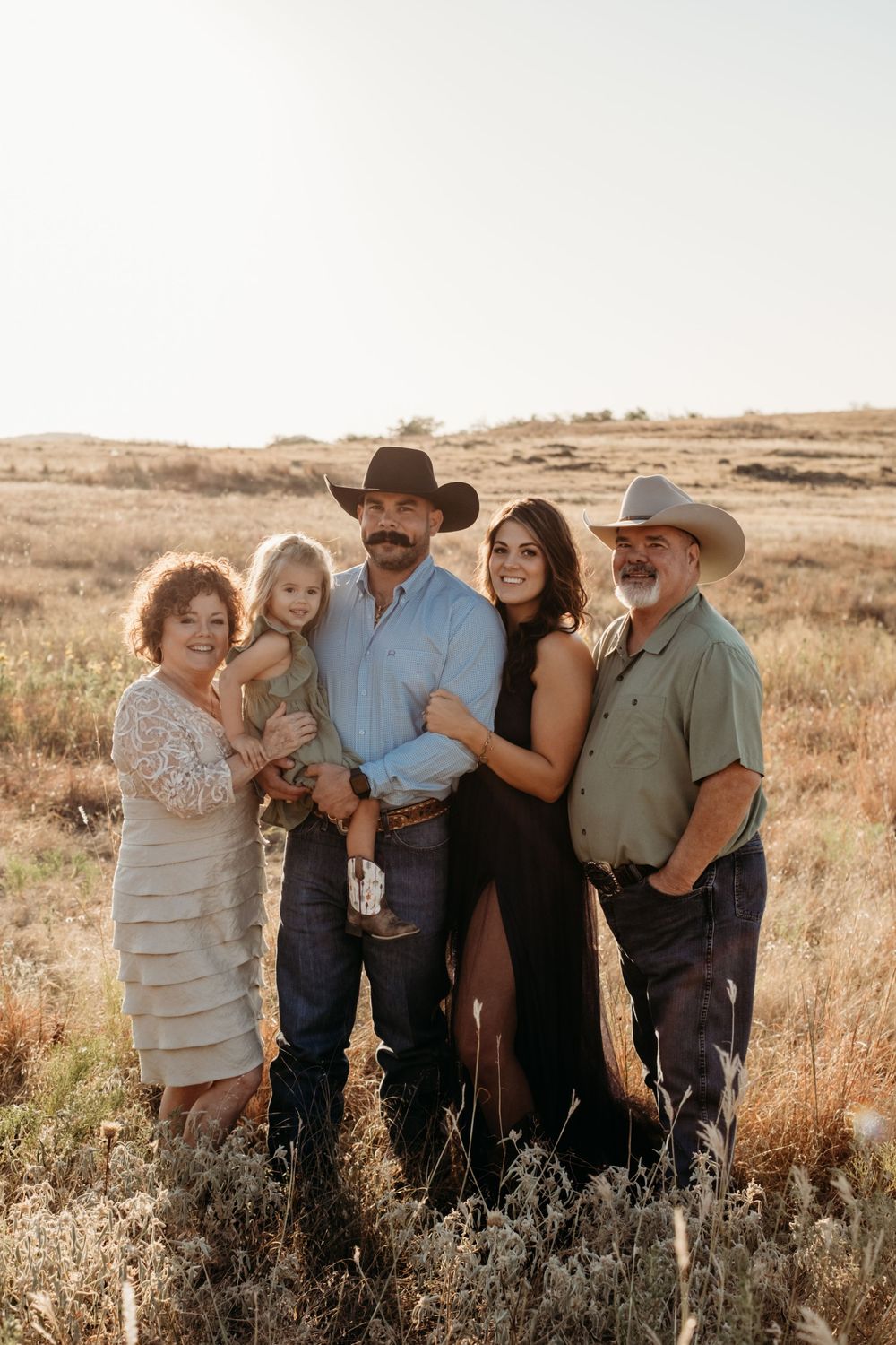 A group wearing western attire gathers together in a rustic field during golden hour.