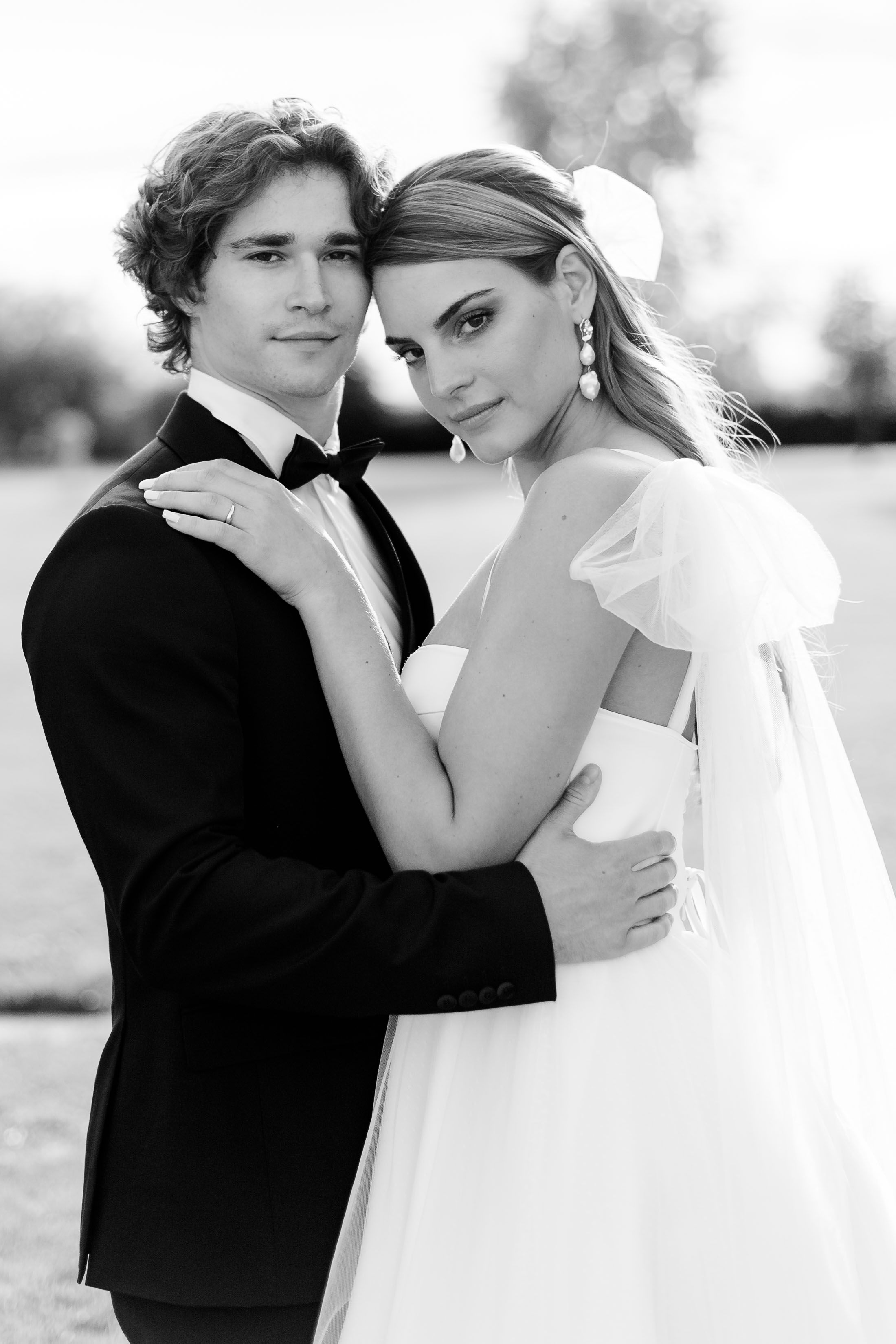 Bride and groom in the garden of their French destination wedding. She is wearing a flowy gown with bows and tulle. Her hair is tied back.