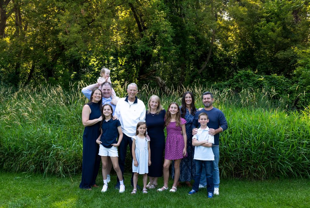 Family group portrait outdoors in summer with trees and grass in background.