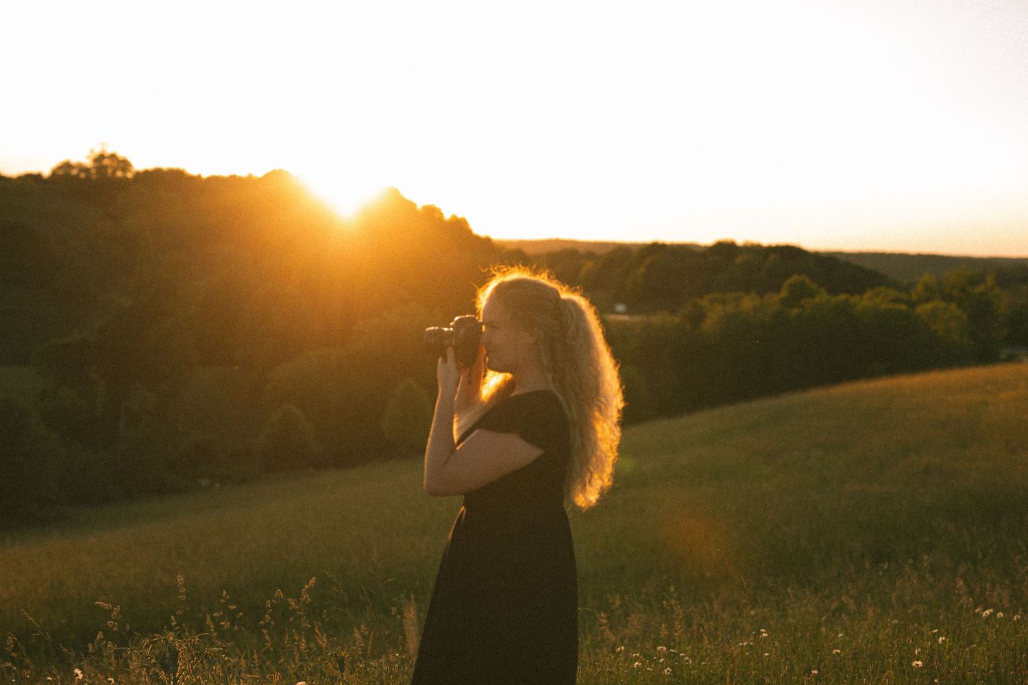 Female photographer captures photos in a golden field during a stunning sunset in rolling countryside.