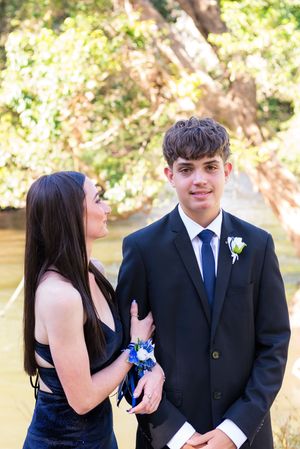 A couple shares playful moments in formal attire with a blue boutonniere and corsage at an outdoor event.
