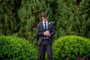Wedding guests in formal attire standing among green hedges and gardens.