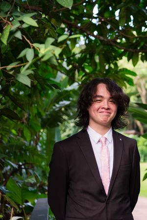 Candid portrait series of person in dark suit and pink tie against leafy background.