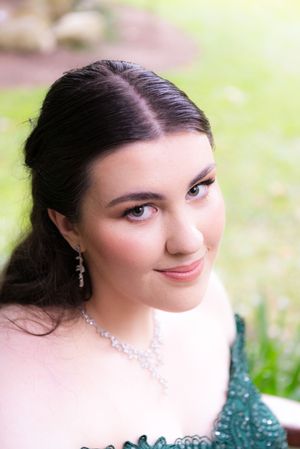 Woman in elegant emerald dress with sparkle detail poses for formal portrait.