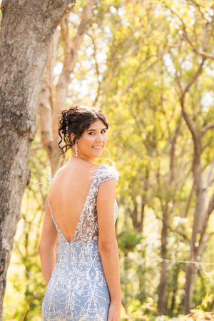 Woman in blue floral dress poses in sunlit wooded area during golden hour photo session.