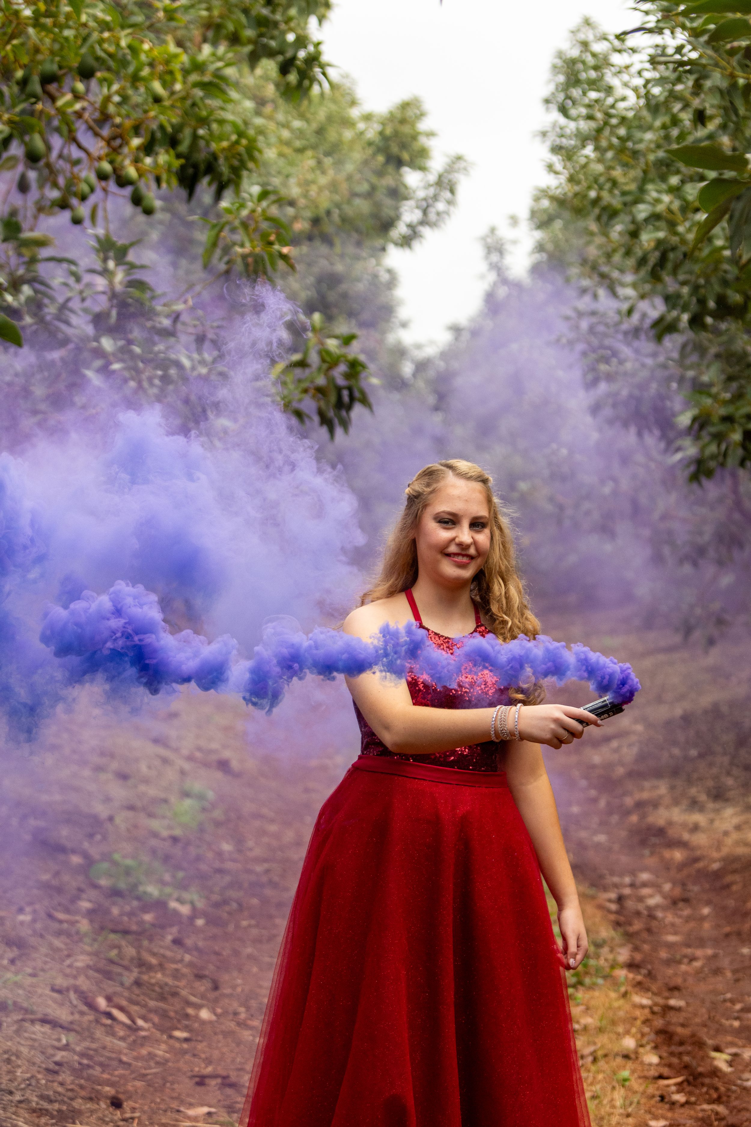 Purple smoke bombs create dramatic effects with a red formal dress in an outdoor photo session.