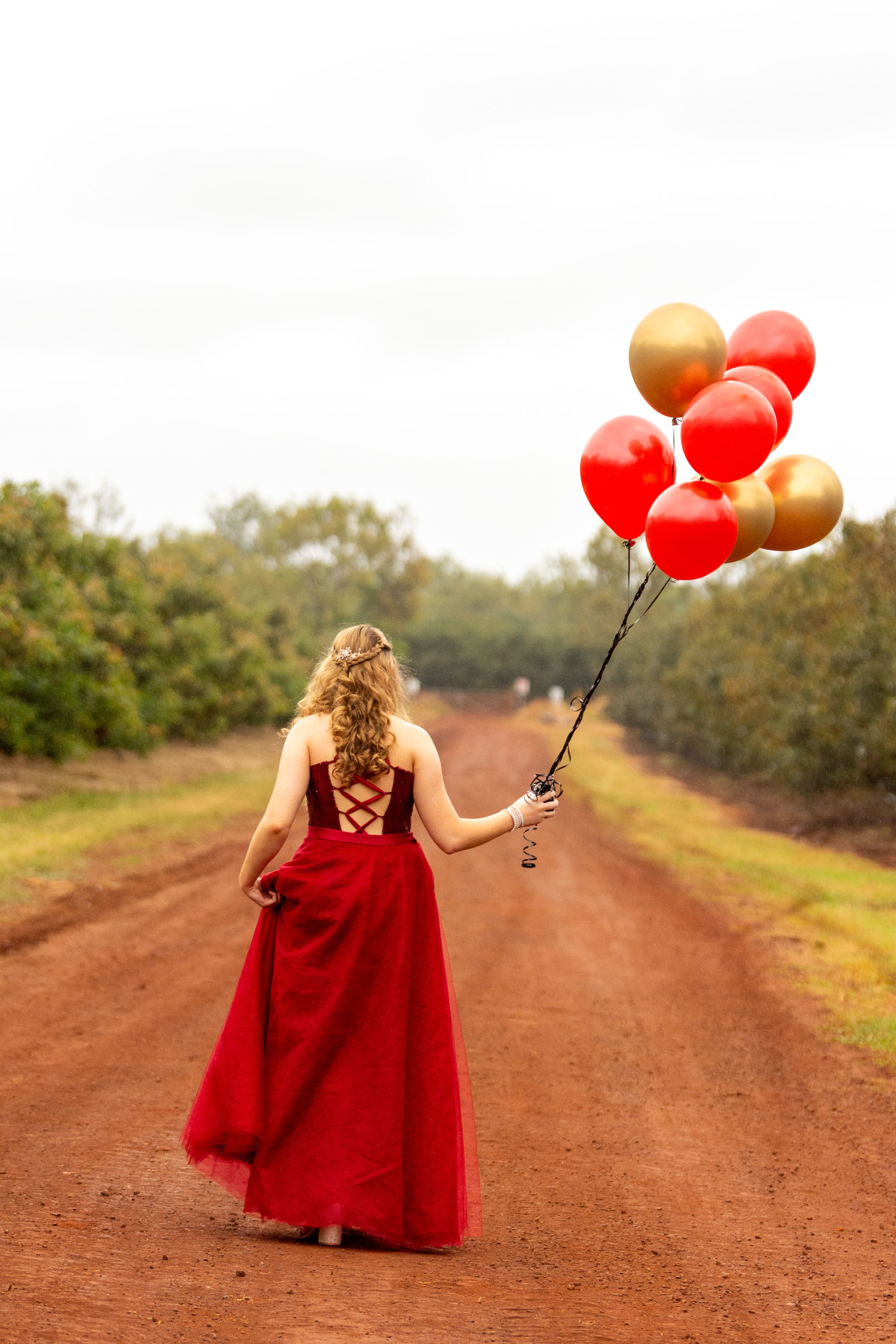 A red formal dress and balloons create a whimsical scene on a dirt path.