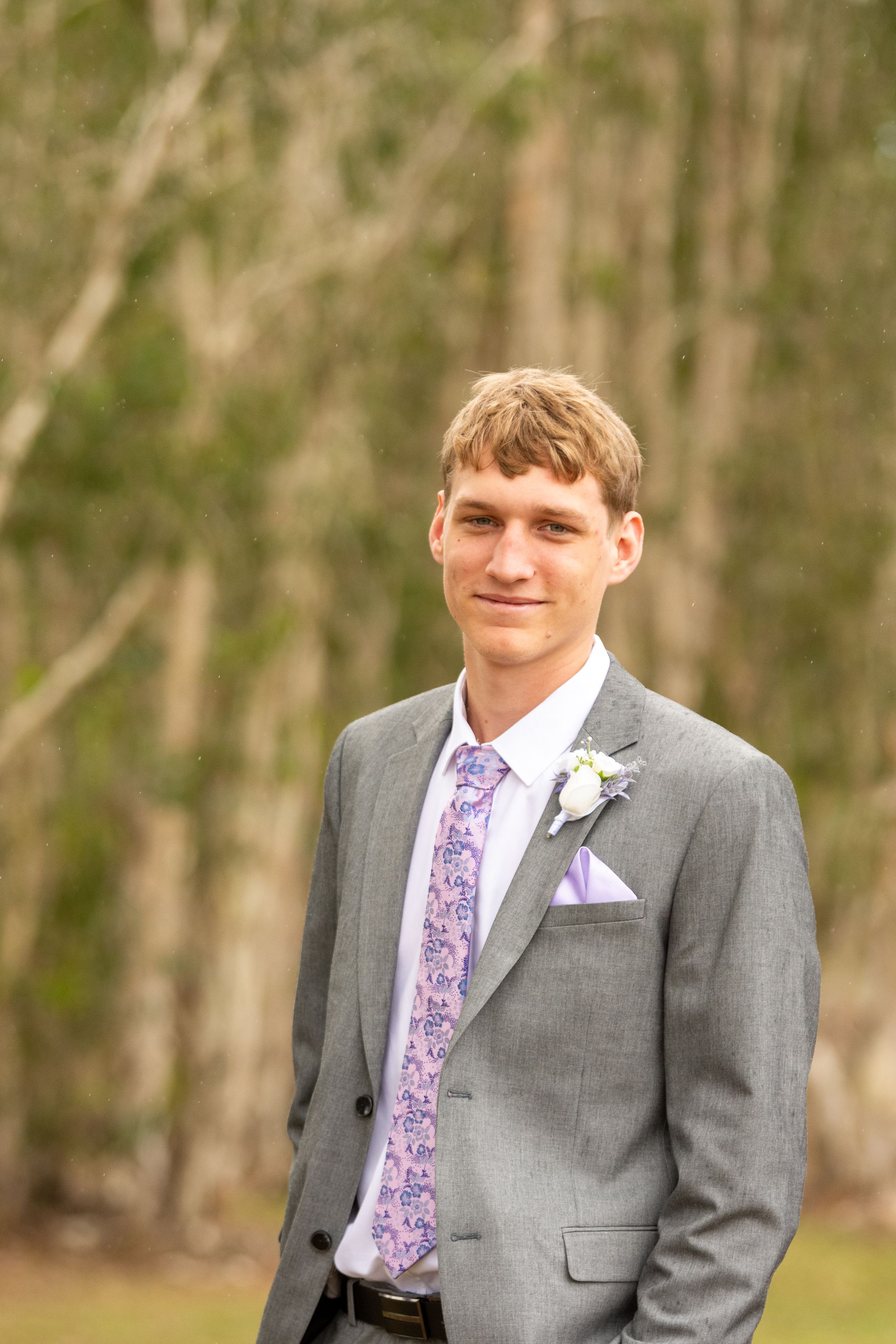 Groom in gray suit with purple tie smiles during outdoor wedding photos.