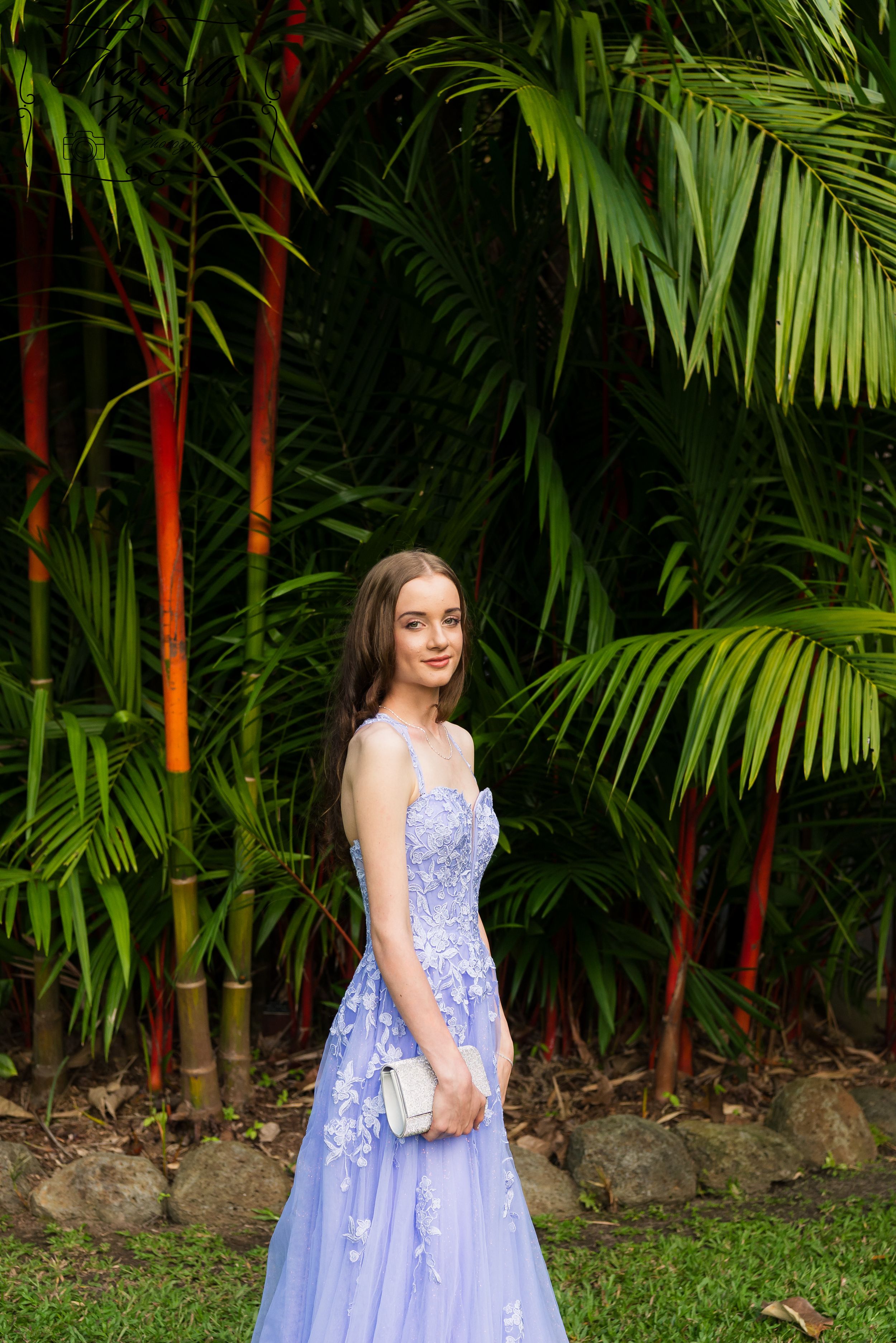 A floral lavender ballgown is showcased against a backdrop of palm trees and greenery.