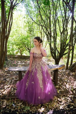 Purple ballgown with gold embellishments photographed in a forest setting.