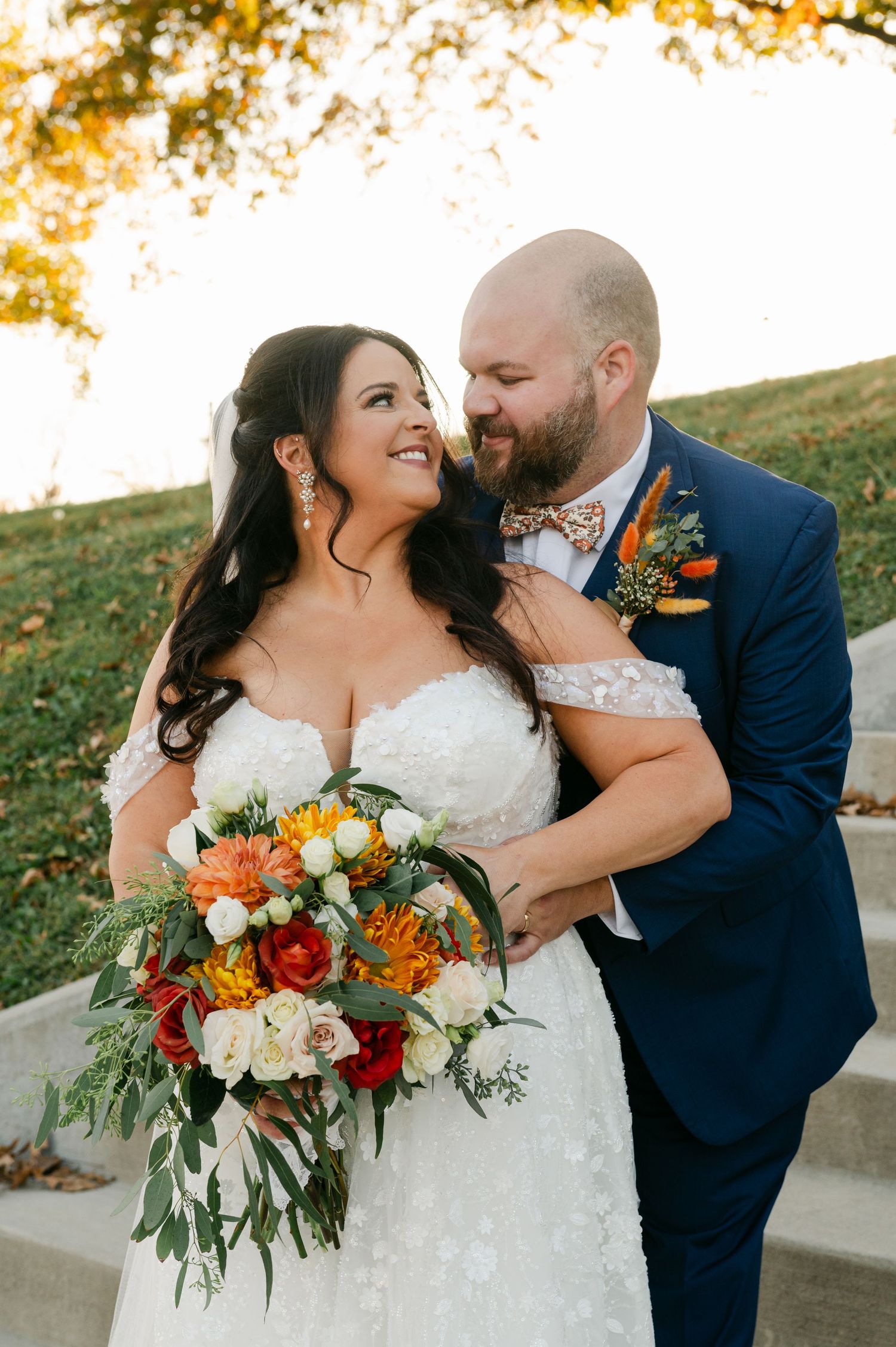 A bride and groom share a romantic moment with a vibrant fall bouquet outdoors.