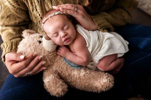 A sleeping newborn baby wrapped in a cozy white blanket nestles against a soft teddy bear.