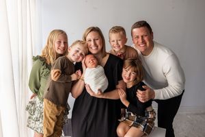 Family members embrace and laugh together during a candid photo session against a white wall background.