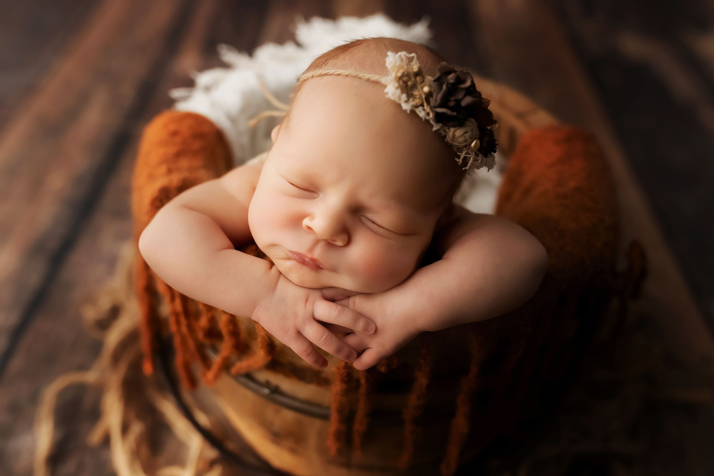Sleeping newborn rests peacefully on rustic brown blanket wearing delicate floral headband.