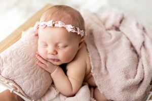 Newborn baby sleeping peacefully on soft pink blanket with delicate floral headband.