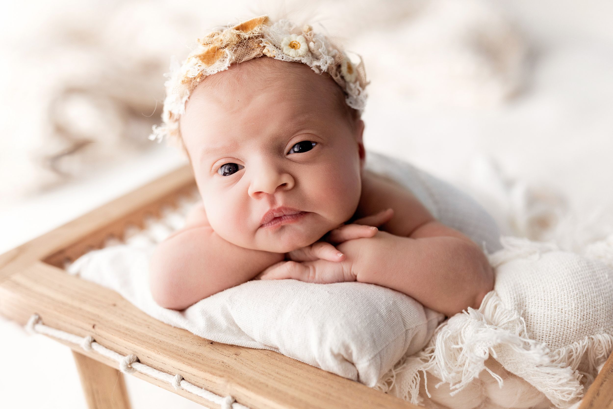 Newborn baby wearing lace headband lying on soft white blankets in professional studio photography setup.