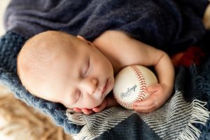 Newborn baby sleeping peacefully with a baseball, captured in a series of black and white lifestyle portraits.