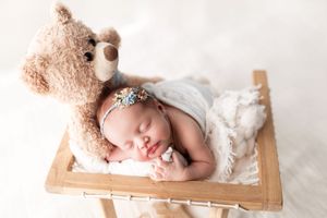 A sleeping newborn wrapped in white lace swaddle rests peacefully in a wooden crate.