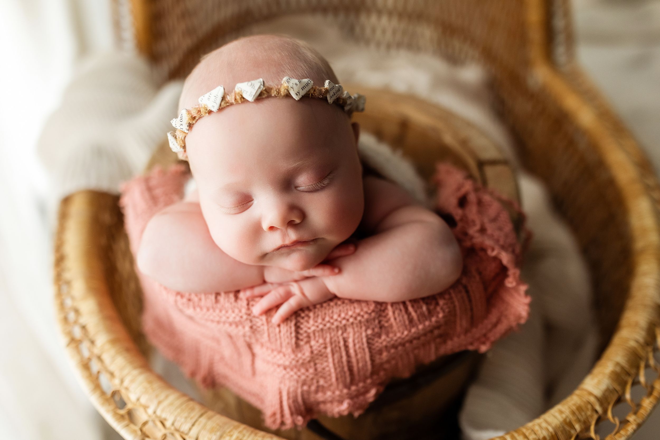 Newborn baby sleeping peacefully in a woven basket wearing a soft pink knit outfit.