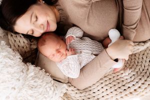 Mother and baby resting together on chunky knit blanket with plush toy.