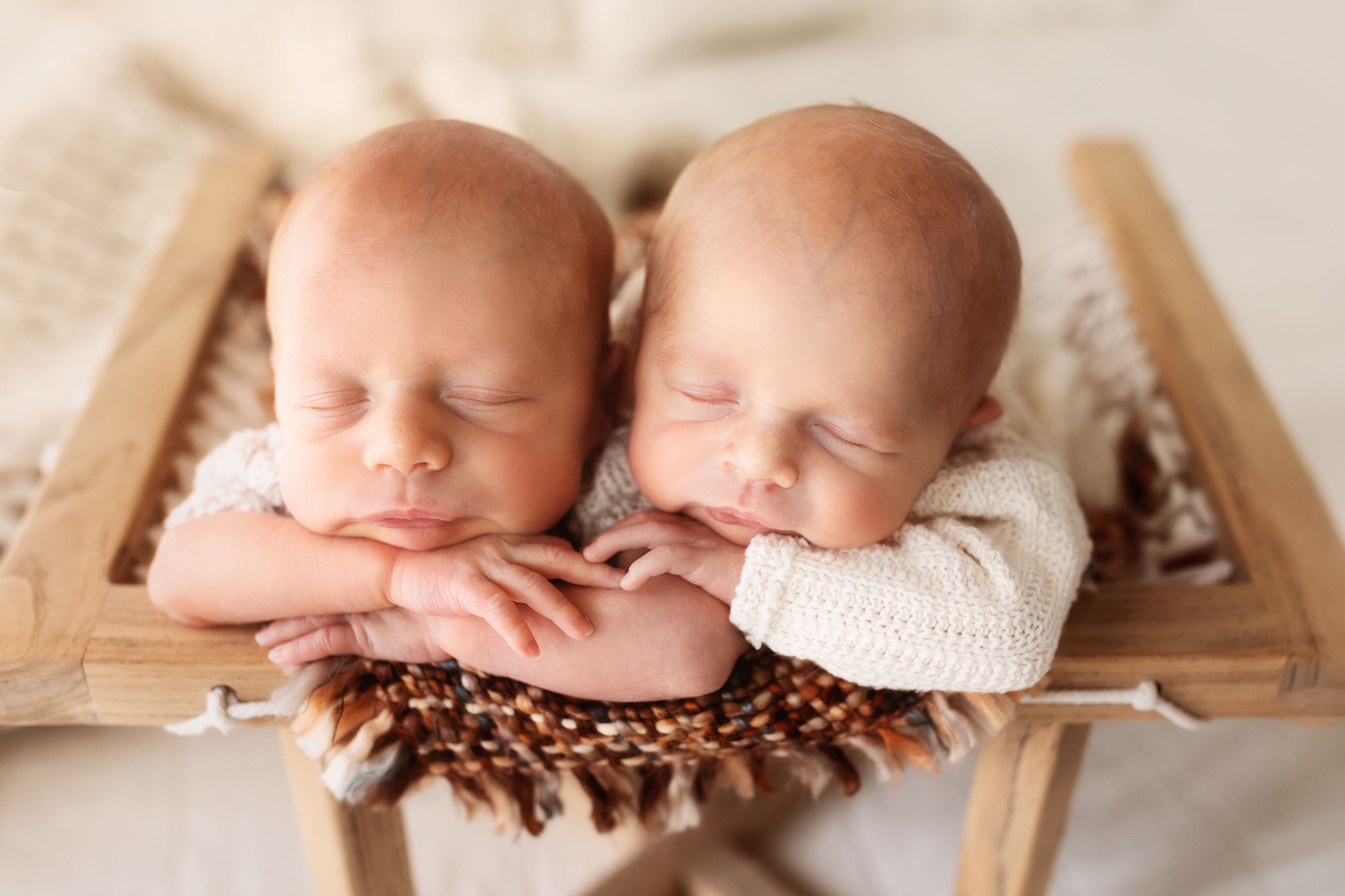 Twin newborns sleeping on wooden surface surrounded by coffee beans.