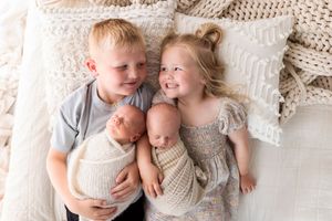 Family portrait on white bedding with young siblings holding twin babies.