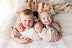 Siblings pose together on white bedding while holding twin babies.
