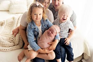 Family lounging together on couch with knit blanket in casual denim outfits.