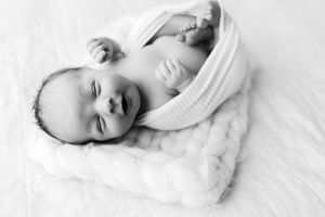 A collage of four monochrome photos showing a newborn baby sleeping peacefully in white blankets.