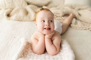 Sweet infant lying on soft white bedding and blankets with a happy expression.