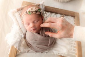 Professional newborn photo with tan wrap and textured cream backdrop.
