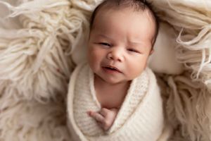 Newborn sleeping peacefully on textured cream blanket in professional studio setting.