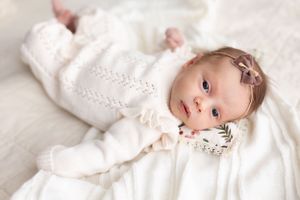 Elegant newborn portrait in white outfit against light backdrop.