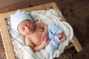 Sleeping newborn in a soft blue hat rests peacefully in a wooden box lined with white fabric.