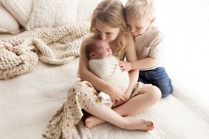 Family snuggling together on couch with knit blanket in soft natural light.