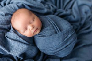 Dreamy newborn portrait in blue wrap against matching textured backdrop.
