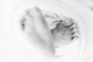 Close-up black and white image of tiny newborn feet wrapped in soft fabric.