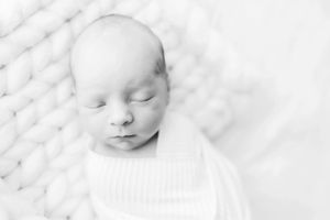 Black and white portrait of peaceful sleeping newborn on textured white blanket.