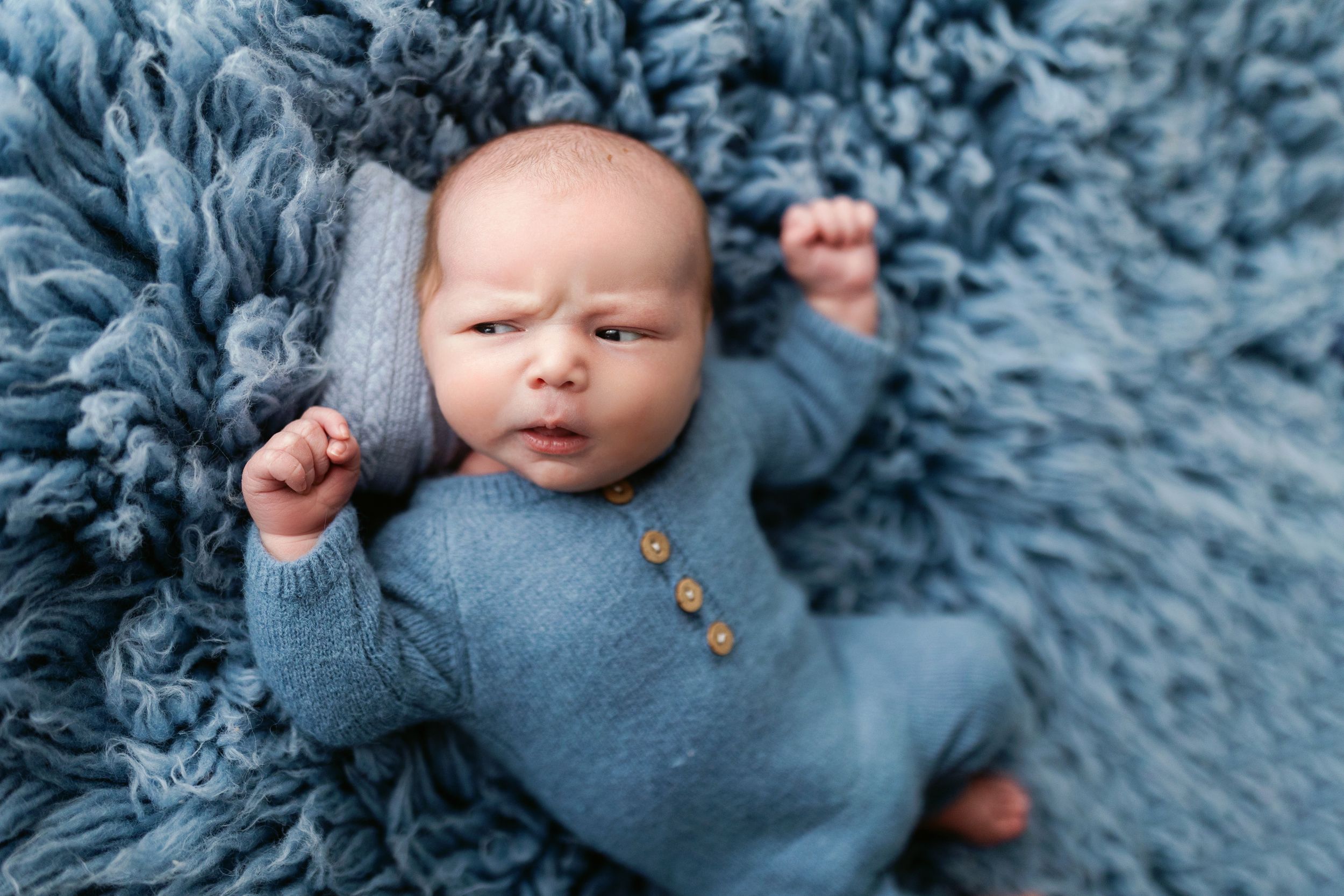 Artistic newborn photo on blue textured blanket wearing knit outfit.