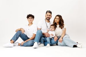 Family of four in white tops and jeans posing together on white background for a studio portrait photo.