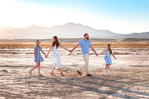Family of four holding hands walking through a sunny desert landscape with mountains in the background.